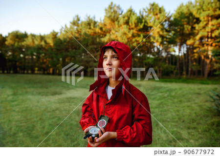A boy in a red windbreaker against the backdrop of a forest with a compass in his hand. A boy in a red windbreaker against the backdrop of a forest with a compass in his hand. 90677972