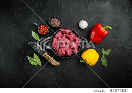 Beef stew prepared  for goulash cooking with sweet bell pepper, in cast iron frying pan, on black stone background, top view flat lay, with copy space for text 90679884