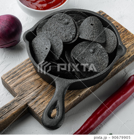 Black crispy potato chips, in cast iron frying pan, on white stone surface Black crispy potato chips, in cast iron frying pan, on white stone surface 90679905