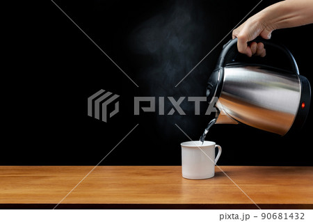 pouring water from kettle water boiler into a cup with smoke on wood table and black background pouring water from kettle water boiler into a cup with smoke on wood table and black background 90681432