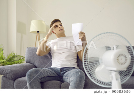 Sweaty man feels bad because of terrible heat sitting at home in front of fan during hot summer days Sweaty man feels bad because of terrible heat sitting at home in front of fan during hot summer days 90682636