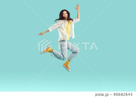 Cheerful excited young woman having fun and fooling around jumping high on light blue background. Cheerful excited young woman having fun and fooling around jumping high on light blue background. 90682643