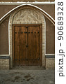 Wooden double-leaf door with an oval brick frame on the facade of an adobe house along a narrow street  of the ancient city of Yazd. 90689328