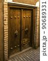 An old double-leaf wooden front door framed with brick on the wall of an adobe house in the ancient adobe city of Yazd. 90689331