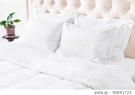 Bedroom with bed, white bedding, and bedside table. White pillows, duvet and duvet case on bed with beige headboard. 90691723