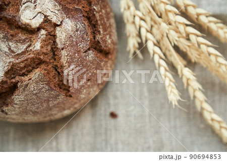 Top view of freshly baked rye bread on a yeast-free starter and on a mixture of whole grain, rye and wheat flour. It lies on a napkin, next to a dried flower with grains. Selective focus. Top view of freshly baked rye bread on a yeast-free starter and on a mixture of whole grain, rye and wheat flour. It lies on a napkin, next to a dried flower with grains. Selective focus. 90694853