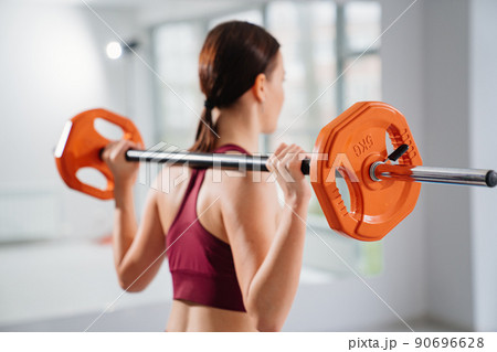 view from the back. a slender woman does exercises with dumbbells in the gym.  90696628