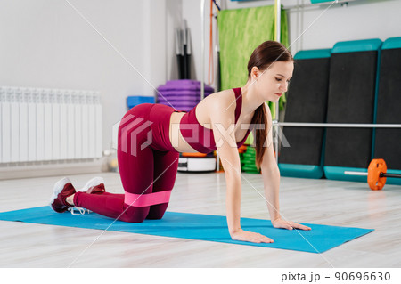 a woman in a tracksuit does elevation legs with gymnastic elastic bands on a mat 90696630