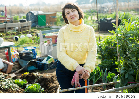 Young woman in a yellow sweater treats weeds in the garden 90699058