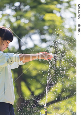 夏の公園で水遊びしている可愛い小学生の女の子の姿 90699489