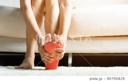 Asian woman sitting on sofa feeling pain in her foot at home 90700826