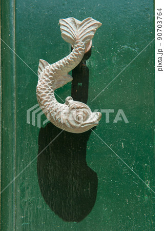 Close-up view of the fish shaped knocker on a green wooden door Close-up view of the fish shaped knocker on a green wooden door 90703764