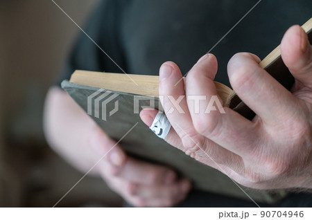 A man is reading a book while holding it in his hands. The first phalanx of his pinky finger is wrapped in white ribbon. A smiling face is painted on the bandage. A man is reading a book while holding it in his hands. The first phalanx of his pinky finger is wrapped in white ribbon. A smiling face is painted on the bandage. 90704946