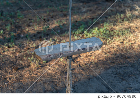 Empty single-rope swing on a rope. Wooden swing and rope with a knot. Close-up. Selective focus. Empty single-rope swing on a rope. Wooden swing and rope with a knot. Close-up. Selective focus. 90704980