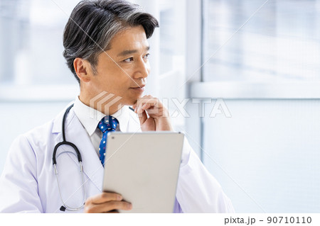 施設内でタブレットPCを持って立っている白衣の医師 90710110