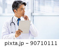 施設内でタブレットPCを持って立っている白衣の医師 90710111