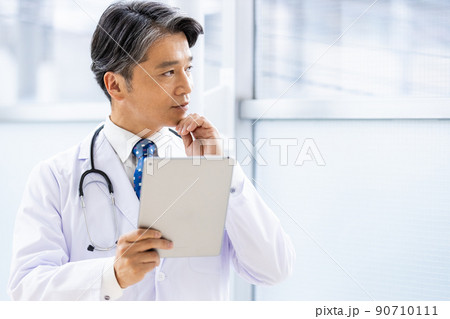 施設内でタブレットPCを持って立っている白衣の医師 90710111