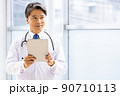 施設内でタブレットPCを持って立っている白衣の医師 90710113