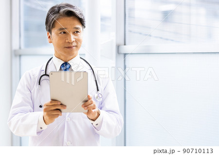 施設内でタブレットPCを持って立っている白衣の医師 90710113