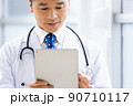 施設内でタブレットPCを持って立っている白衣の医師 90710117