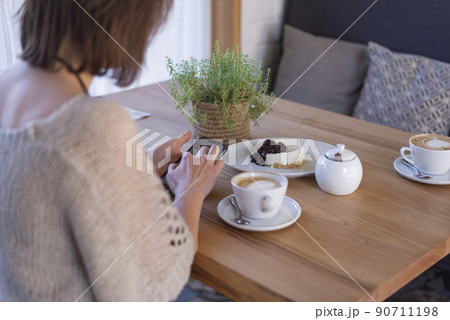 Woman at table in cafe uses mobile phone. Business woman with phone in her hands during breakfast in coffee shop. 90711198