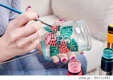 A girl paints a glass jar with stained glass paints A girl paints a glass jar with stained glass paints 90711984