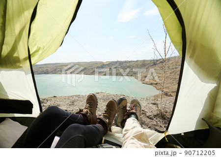 POV of two unrecognizable young women relaxing in camp tent on spring day enjoying beautiful view of quarry lake POV of two unrecognizable young women relaxing in camp tent on spring day enjoying beautiful view of quarry lake 90712205