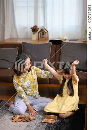 Happy mature grandmother having fun playing with cute little preschooler granddaughter in living room. Multi generational, family and love concept 90712691
