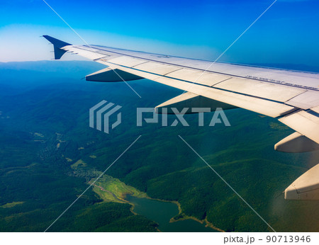 View of airplane wing, blue skies and green land during landing. Airplane window view. View of airplane wing, blue skies and green land during landing. Airplane window view. 90713946