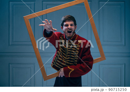 Creative portrait of young shouting man in image of medieval hussar posing isolated on dark blue background. Retro style, comparison of eras concept. 90715250