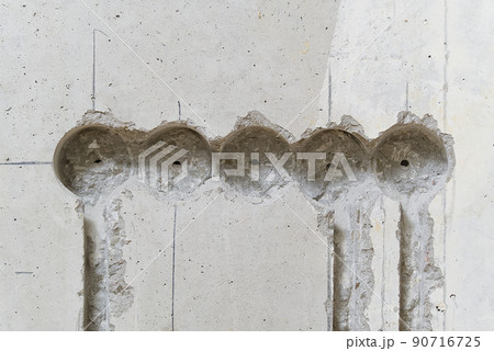 Holes in a concrete wall for installing plastic boxes under sockets. installation of sockets in a concrete wall and wiring. Holes in a concrete wall for installing plastic boxes under sockets. installation of sockets in a concrete wall and wiring. 90716725