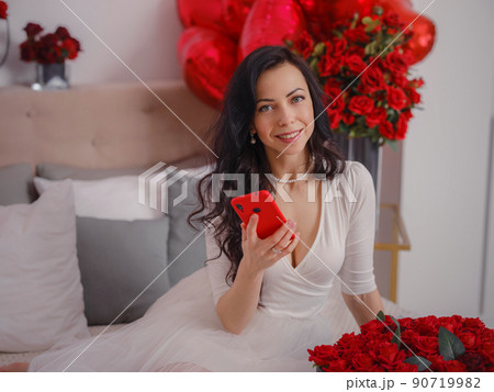 young woman in white dres is sitting on bed. 90719982