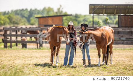 Two cowgirls meet their paint horses on a ranch on a sunny day Two cowgirls meet their paint horses on a ranch on a sunny day 90721740
