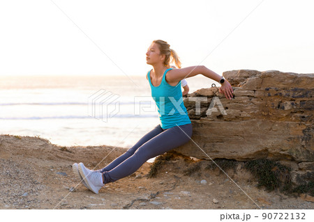 Young adult fit woman doing triceps dips exercises during outdoor cross training workout. Fitness female model training summer day near ocean beach. 90722132