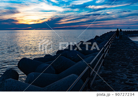 夕暮れの海を防波堤から眺めるカップル 夕暮れの海を防波堤から眺めるカップル 90727234
