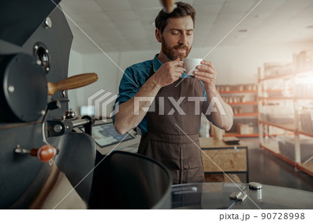 Business owner inhaling aroma of fresh made coffee on the background of roasting coffee machine Business owner inhaling aroma of fresh made coffee on the background of roasting coffee machine 90728998