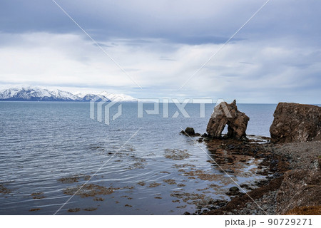 Rock formations at seashore with snowcapped mountain in background against sky 90729271