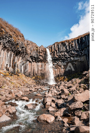 Beautiful cascades of Svartifoss waterfall and flowing stream against blue sky 90729511