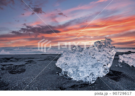 Beautiful ice crystal on black sand of Diamond beach against cloudy sky at sunset Beautiful ice crystal on black sand of Diamond beach against cloudy sky at sunset 90729617