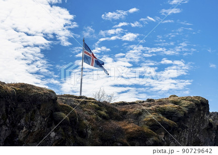 Icelandic flag waving on rocky cliff against blue cloudy sky Icelandic flag waving on rocky cliff against blue cloudy sky 90729642