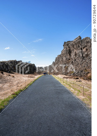 Tourists walking on road amidst cliffs against sky at Thingvellir national park Tourists walking on road amidst cliffs against sky at Thingvellir national park 90729644