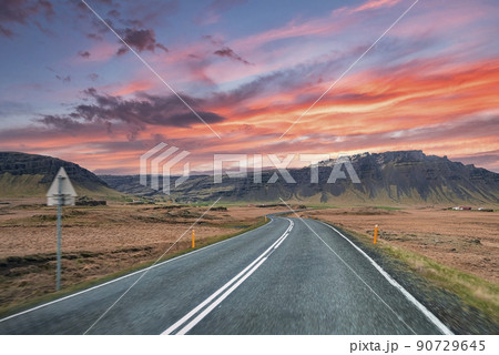 Empty highway leading towards mountain range against cloudy sky during sunset 90729645
