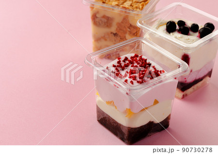 Mousse desserts in square plastic boxes with different toppings on pink table 90730278