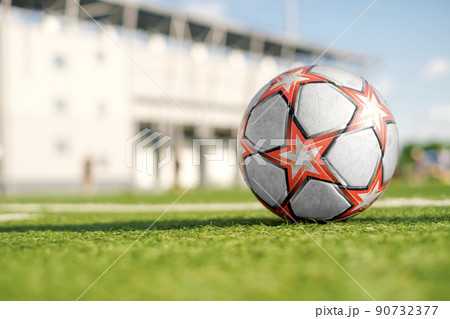 Soccer ball with red stars on the green artificial grass of the football field in the stadium. Summer sunny day. Youth Sports soccer School. Background with copy space Soccer ball with red stars on the green artificial grass of the football field in the stadium. Summer sunny day. Youth Sports soccer School. Background with copy space 90732377