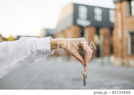 Woman hand holds the keys to an apartment against the background of buildings. Woman hand holds the keys to an apartment against the background of buildings. 90734096