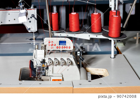Industrial sewing machine with red spools of thread on a dark workshop background. 90742008