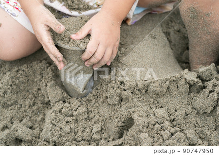 Kid holds and plays sand in the plastic cup on the beach. 90747950