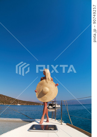 Beautiful young blond woman in bikini standing on catamaran bow at sunny summer day 90749257