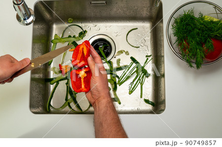 man cutting sweet pepper with a knife over the sink 90749857