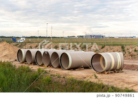 Stack of big frp composite fiberglass plastic sewage pipes at warehouse construction site near Leipzig Halle airport against blue sky background. Highway road construction infrastructure earthworks 90749861